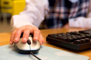 A young person with their hand on a mouse. Using it to navigate through a website.